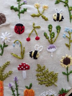 embroidered flowers and bugs on a white cloth with green stems, daisies, ladybugs, and mushrooms