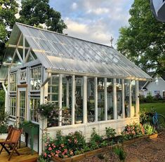 a small greenhouse with lots of windows and flowers in the front yard, next to a wooden deck