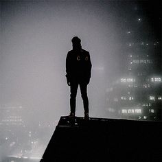 a man standing on top of a roof in the foggy city at night time