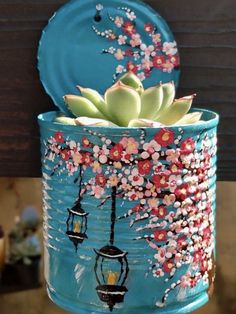 a blue tin can with succulents and flowers painted on it, hanging from a wooden fence