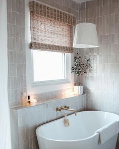 a white bath tub sitting under a window next to a lamp and a light fixture