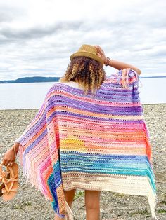 a woman wearing a colorful crochet ponchy on the beach with her back to the camera