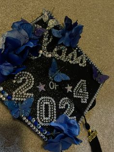 a graduation cap decorated with blue flowers and beads on the floor next to a tassel