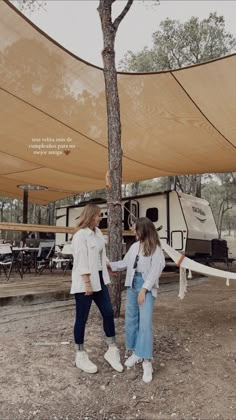 two girls standing under an awning next to a tree