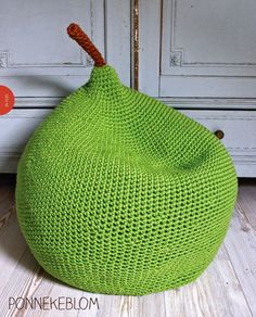 a green knitted bean bag sitting on top of a wooden floor next to a white cabinet