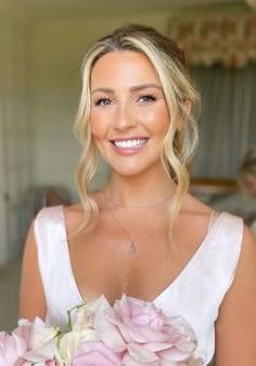 a woman in a white dress holding a bouquet of pink flowers and smiling at the camera