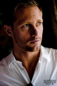 a close up of a person wearing a white shirt and looking at the camera with an intense look on his face