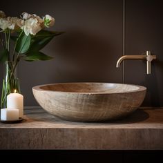 a large wooden bowl sitting on top of a counter next to a candle and flowers