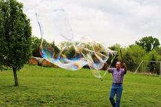 a man standing on top of a lush green field flying a large bubble filled kite