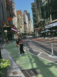 two women standing on the side of a street next to tall buildings and traffic lights