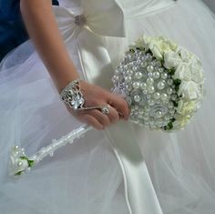 a woman in a wedding dress holding a bridal bouquet with pearls and flowers on it