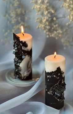 two black and white candles sitting next to each other on top of a cloth covered table