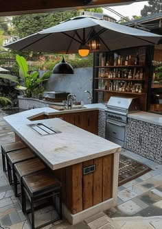 an outdoor kitchen with tables and umbrellas over the grill area, surrounded by stone pavers