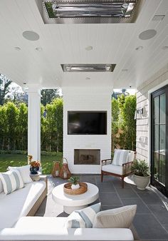 an outdoor living area with white furniture and a flat screen tv mounted above the fireplace