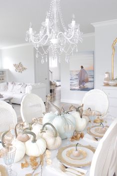 a dining room table is set with white pumpkins and gold place settings for dinner