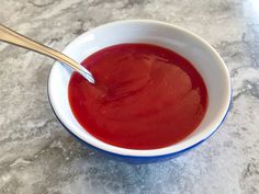 a white bowl filled with red liquid on top of a counter next to a wooden spoon