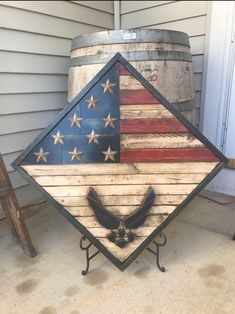 an american flag made out of wood sitting on the side of a house next to a barrel