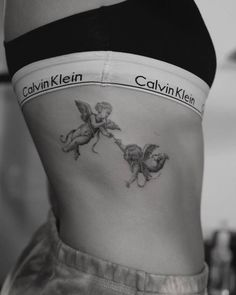 a woman's stomach with two cherubs tattooed on the side by her