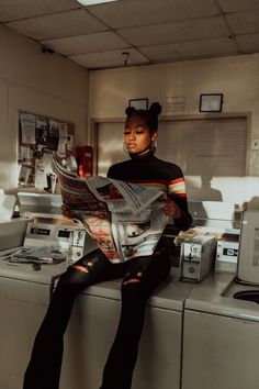 a woman sitting on top of a dryer next to a washing machine holding a newspaper