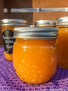 three jars filled with orange liquid sitting on top of a purple table cloth