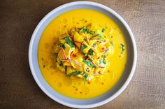 a white bowl filled with yellow soup and garnished with green leafy garnish