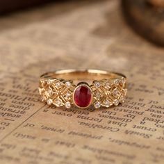 a gold ring with a red stone surrounded by white diamonds on top of an old book