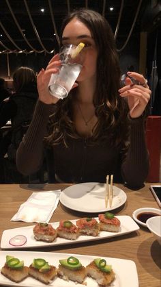 a woman sitting at a table drinking water and eating sushi