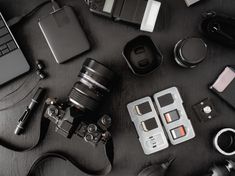 an assortment of electronic devices and cameras on a black table next to a laptop computer