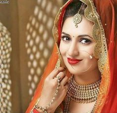 a woman wearing a red and gold bridal outfit with jewelry on her head, smiling at the camera