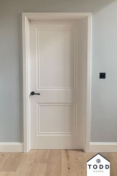 an empty room with a white door and wood flooring on the side, in front of a gray wall