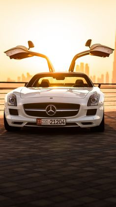 a white mercedes sports car parked in front of a large cityscape at sunset