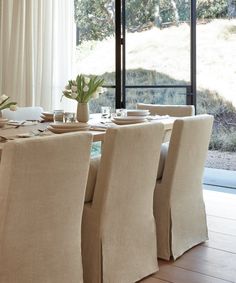 a dining room table with beige chairs next to a large window overlooking the mountains and trees