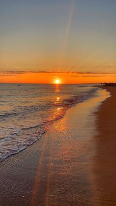 the sun is setting over the water at the beach with waves coming in to shore