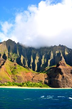 the mountains are covered with green vegetation and clouds in the sky over the blue water