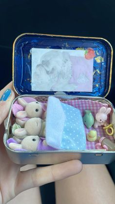 a person holding an open tin container with stuffed animals in it and a baby's photo on the lid