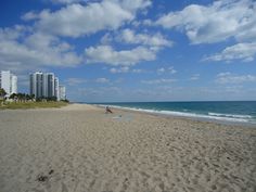 people are on the beach in front of some buildings and blue skies with white clouds