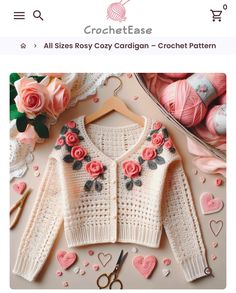 a knitted sweater with roses and hearts on it, next to yarn balls and scissors