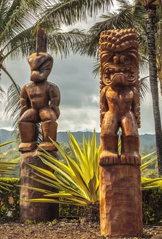 two carved wooden totemas sitting next to each other in front of palm trees