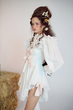 a woman in a white dress is standing next to hay bales with her hands on her hips