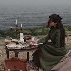 a woman sitting at a table with books and candles in front of the water on a foggy day