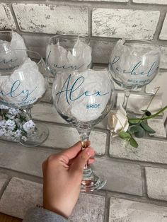 a person holding a wine glass in front of a brick wall with white flowers on it