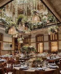 a dining room with tables and chairs covered in greenery, surrounded by chandeliers