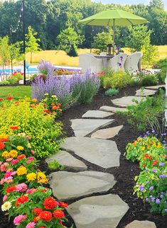 a garden with flowers and an umbrella in the middle of it's path that leads to a swimming pool