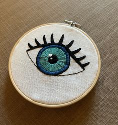 an embroidered eyeball with blue and green eyes sits on top of a beige surface