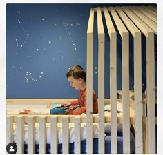 a young boy sitting in his crib reading a book with the stars above him