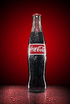 a coca - cola bottle sitting on top of a table covered in water drops and red background