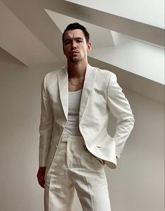 a man in a white suit standing next to a wall with his hands on his hips