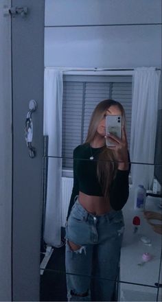 a woman taking a selfie in front of a mirror wearing ripped jeans and a crop top