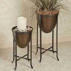 two metal planters with plants in them and a candle on the table next to each other