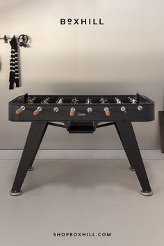 A black outdoor football table with wooden handles placed against a minimalist light colored wall